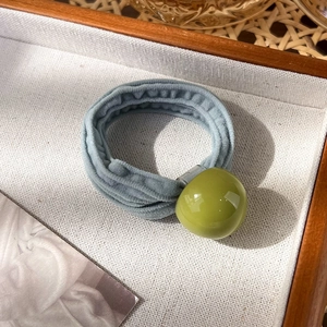 Détail d'un chouchou bleu en velours avec une perle vert olive brillante sur plateau
