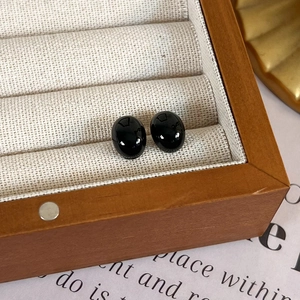 Detailed view of polished black oval stud earrings displayed in a premium wooden jewelry box