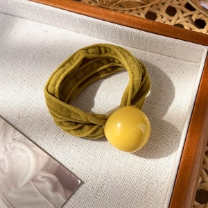 Détail d'un chouchou en velours vert moutarde avec une grande perle jaune sur un plateau