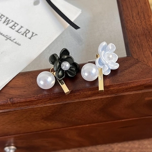 Asymmetric gardenia flower earrings with pearls and gold metal drops on a wooden box
