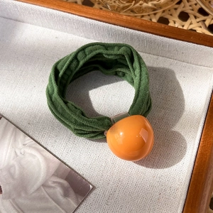 Détail d'un chouchou en velours vert avec une boule de kaki orange sur plateau en toile