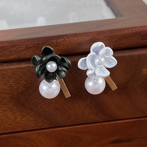 Elegant black and white gardenia pearl drop earrings on a premium wooden jewelry display