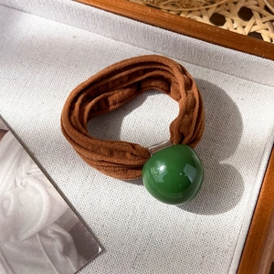 Détail d'un chouchou en tissu marron avec perle vert foncé brillante sur tissu blanc