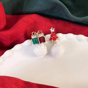 Dettaglio macro di orecchini natalizi asimmetrici con confezione regalo e albero di Natale