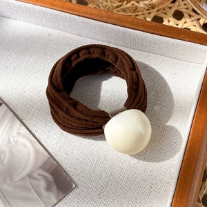 Détail d'un chouchou élastique marron café avec texture plissée et perle décorative blanche