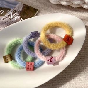 Close-up of five colorful plush hair scrunchies with cute mini girl tags in a white tray