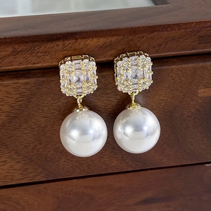 Detail of elegant gold earrings featuring square zircon stones and round white pearls on wood