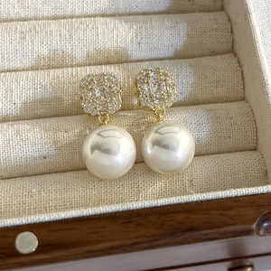 Detailed close-up of gold-plated zircon and pearl drop earrings in a soft beige jewelry box