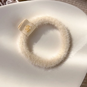 Close-up of a fluffy cream plush scrunchie with a small floral tag in a ceramic dish