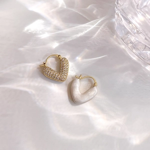 Détail de boucles d'oreilles cœur en or avec émail blanc et pierres de zircon brillant