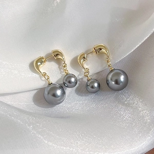 Detailed view of grey double pearl earrings with gold chain on white silk background
