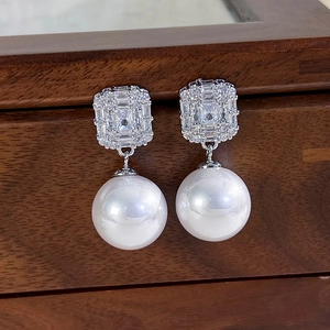 Detail of zircon crystal square stud earrings with round white pearls on a wood surface