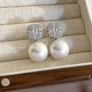 Detail of elegant silver drop earrings featuring square crystal studs and large white pearls