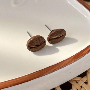 Macro shot of coffee bean earrings with realistic roasted texture on white ceramic plate
