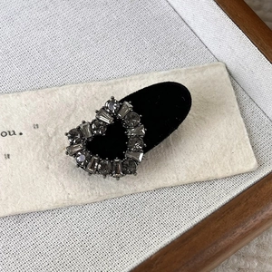Macro view of heart-shaped grey rhinestone hair clip on black velvet base and rustic background