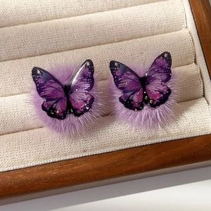 Gros plan sur des boucles d'oreilles papillon en résine violette avec pompons doux