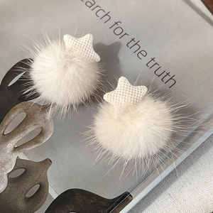 Detailed close-up of soft white plush pom-poms with woven star details on neutral fabric
