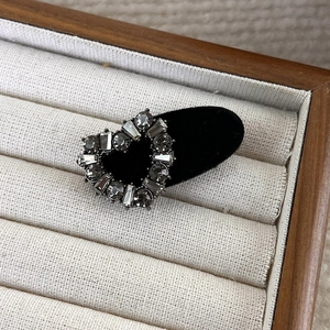 Detailed view of heart-shaped grey velvet hair clip with sparkling rhinestones on fabric
