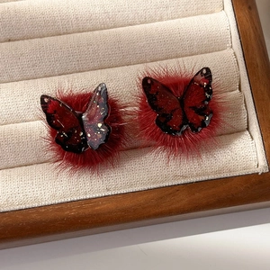 Détail de boucles d'oreilles papillon en peluche rouge avec ailes en résine et flocons d'or