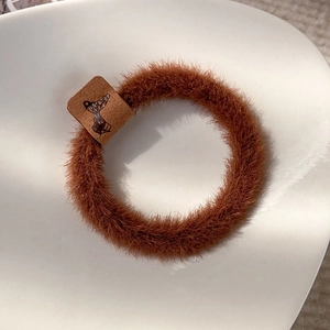 Close-up of brown plush hair tie with butterfly label on a white minimalist tray