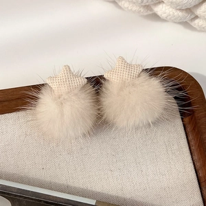 Detail view of plush cream-colored star earrings displayed on a rustic linen tray