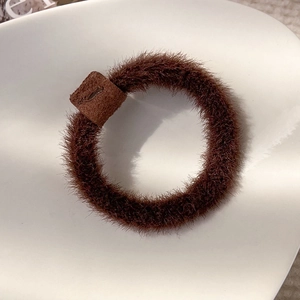 Close-up of fluffy brown plush hair tie with matte leather buckle on white ceramic plate