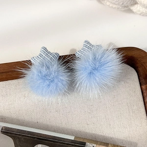 Close-up of plush blue star earrings with soft pom-pom texture and striped fabric detail