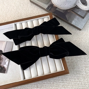 Elegant black velvet bow hair clips with long ribbons on a wooden jewelry display tray