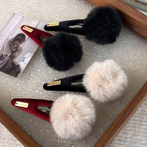 Close-up of four plush pompom hair clips with velvet bases and handmade metal labels