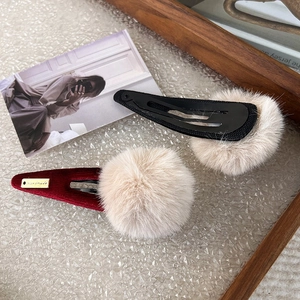 Detail of burgundy corduroy and black hair clips with beige faux fur balls and handmade tag
