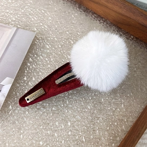 Close-up of a red velvet BB hair clip with a fluffy white pompom and golden handmade tag
