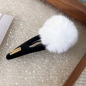Detailed macro of a soft white pom-pom hair clip with golden Handmade metal emblem