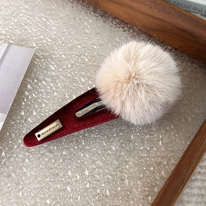 Detail of a plush pompom hair clip with red corduroy and gold handmade charm