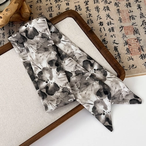 Detail of a silk twilly scarf with black and white ink floral pattern on a wood tray