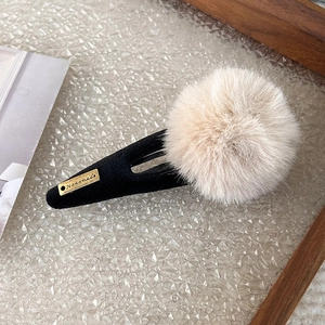 Detail view of plush beige faux fur ball hair clip with golden Handmade metal tag