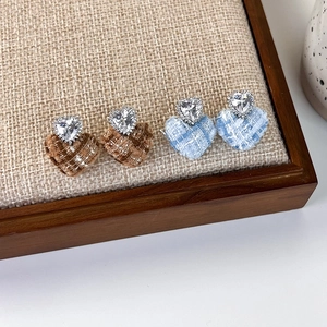 Macro shot of tweed heart earrings featuring sparkling zirconia studs on fabric texture