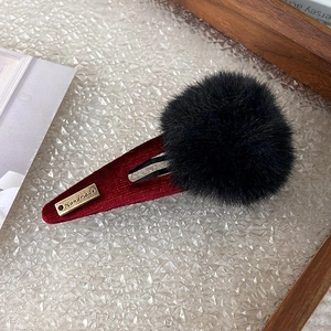 Detail of red corduroy BB clip with large black faux fur pompom and handmade tag