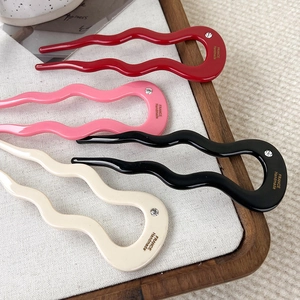 Detail of four acetate wave hairpins in red, pink, black, and cream on a wooden tray