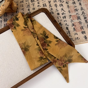 Detail of vintage floral silk twilly scarf elegantly placed on a traditional wooden tray