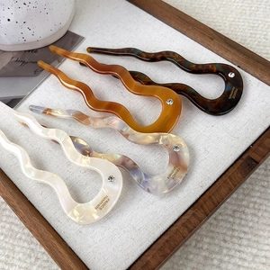 Macro shot of wavy acetate hair sticks in amber and marble patterns with crystal detail