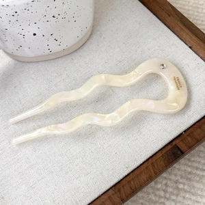 Detailed macro of cream acetate U-shaped hair pin with wave design and diamond accent