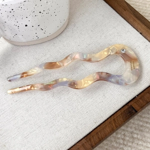 Detail view of wavy acetate hair pin with marble texture and small rhinestone accent