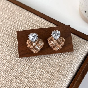 Detail of heart stud earrings featuring sparkling stones and brown plaid tweed fabric