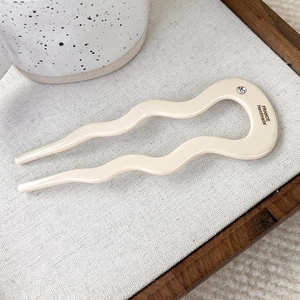 Close-up of cream acetate U-shaped hair pin with wave design and small rhinestone