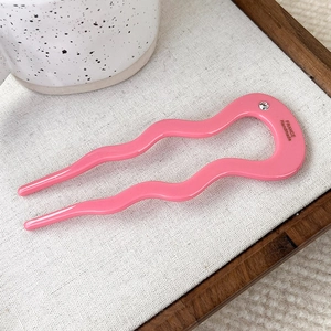 Close-up of pink wavy U-shaped acetate hair pin with sparkling rhinestone detail