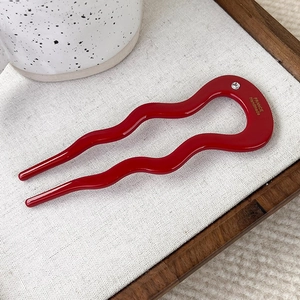 Close-up of wavy red acetate hair pin with sparkling rhinestone and gold lettering
