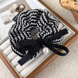 Detail of tweed hair scrunchie with a large black bow and white pearl pendant on a tray