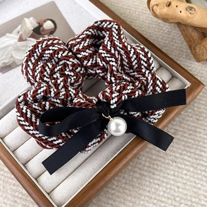 Close-up of a tweed hair scrunchie with a black satin bow and a white pearl accent