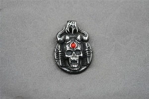 Close-up of gothic skull pendant with bull horns and a red gemstone on a gray surface