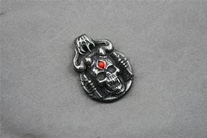 Detail of gothic devil skull pendant with red gem inlay and curved horns on silver base